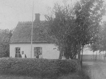 Johanne og Hans ved indkørslen til gården 1928-30. Bag dem Magda og i haven Gerda og sandsynligvis Hans Rasmussen. Indgangen til Stuehuset var fra gården, i nordøst-hjørnet var soveværelset, mod sydøst lå stadsstuen. I midten var hverdagsstuen, og bag det lille vindue i vestenden kammeret, hvor lille Hans overnattede sammen med sin mor. Mod nordvest nær staldlængen lå ”storkøkkenet”.