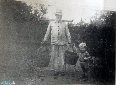 Emil Frederiksen med barnebarnet Poul Emil på frugtplantagen ca, 1950. Frugten blev samlet ind i store kurve. Bemærk åget, som lagde vægten op over skuldrene.